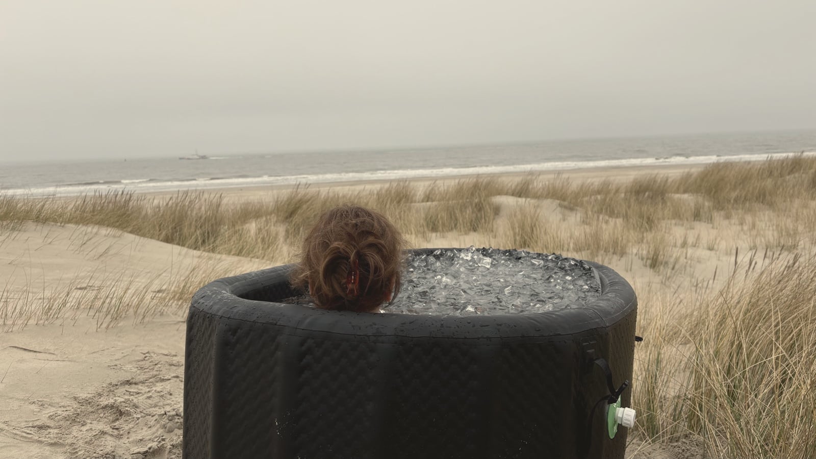 Vrouw in een ijsbad in de duinen op Vlieland, met uitzicht op het strand en de zee.